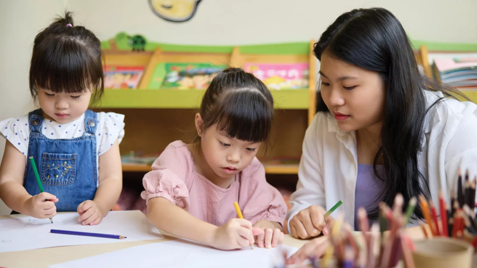 04-Parents-NIEC-Resilience-MAIN A woman and two children engage in drawing on paper, showcasing their resilience and creativity through art.