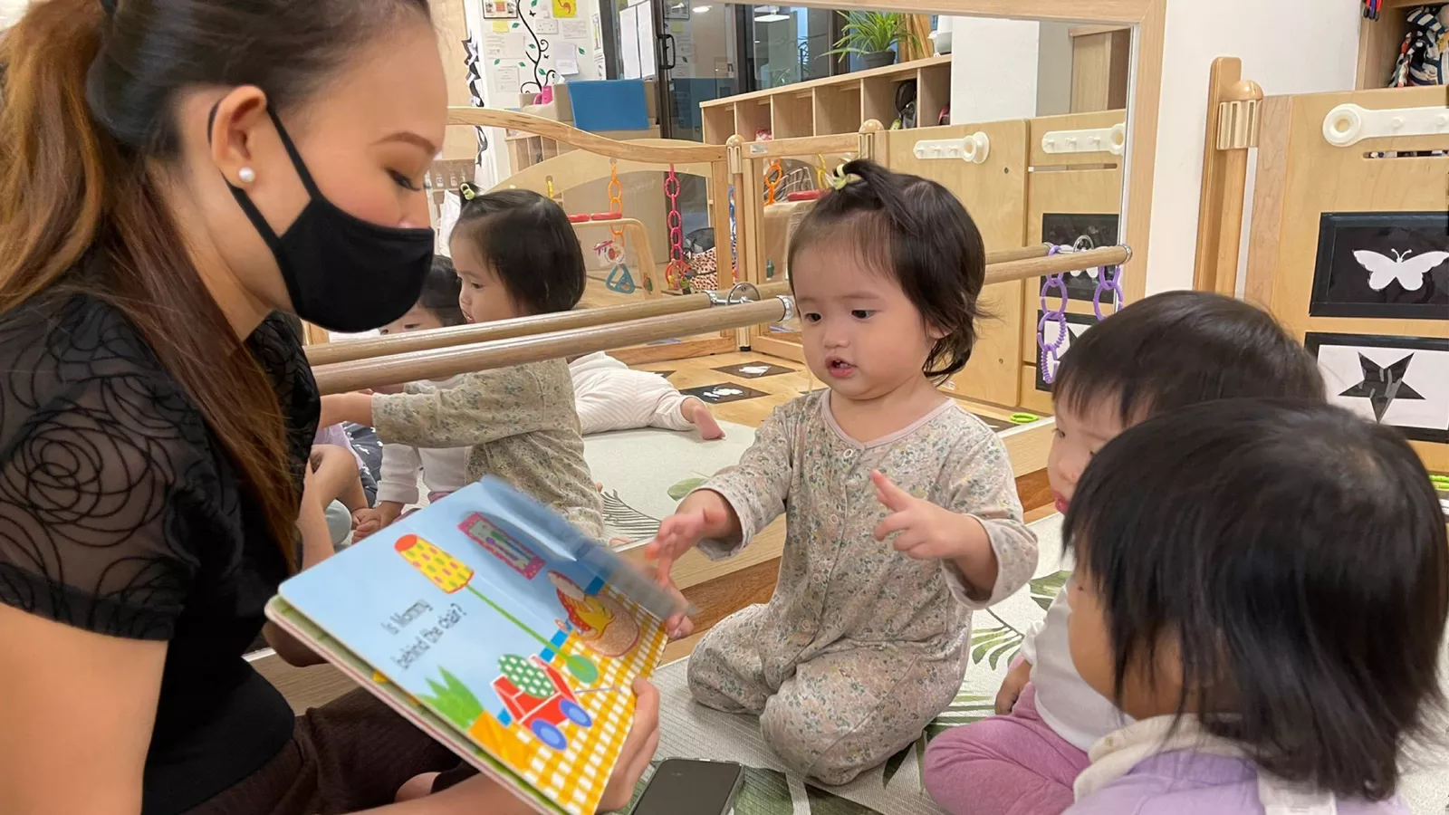 Parents-Stages-Milestones-Infant-care-myths-MAIN An infant educator reads to a group of young children, debunking misconceptions about infant care being unimportant.