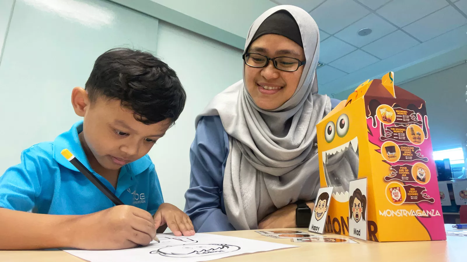 Parents_Stages&Milestones-LSEd-Nor-Jannah-MAIN A child engages in a drawing activity while learning to regulate his emotions, guided by early interventionist Nor Jannah.
